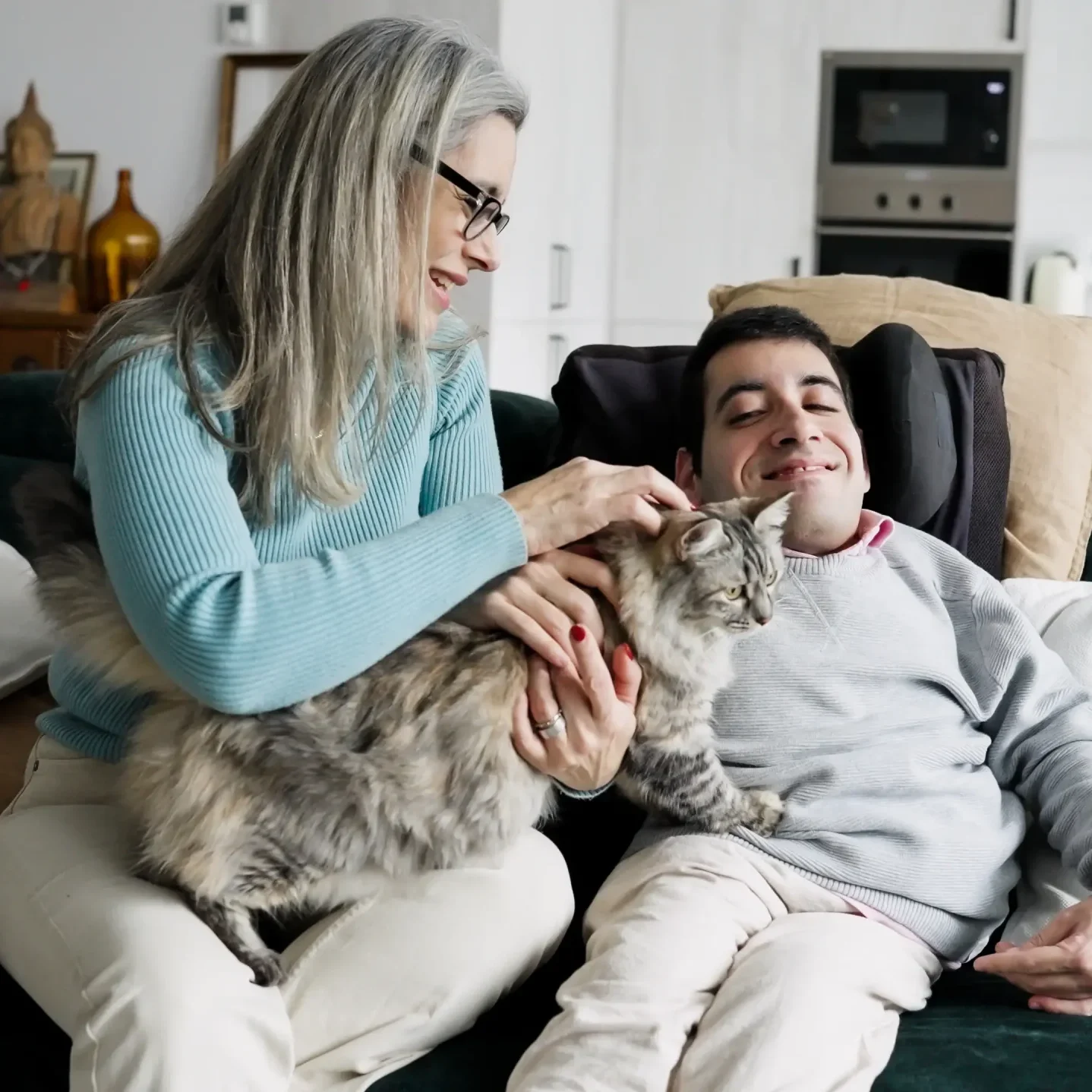 Carer petting a cat with disabled men sitting on sofa
