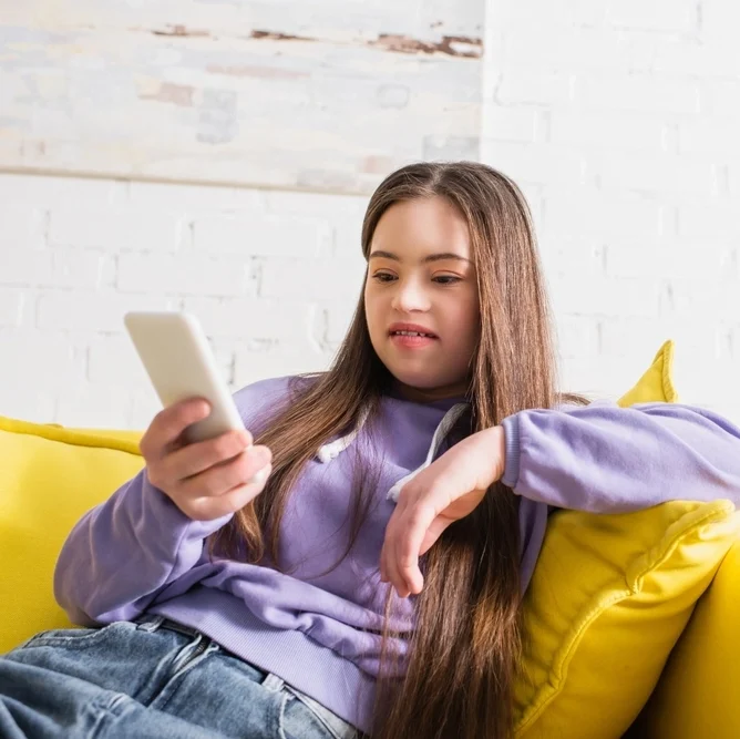 Disabled young girl using phone and sitting on sofa